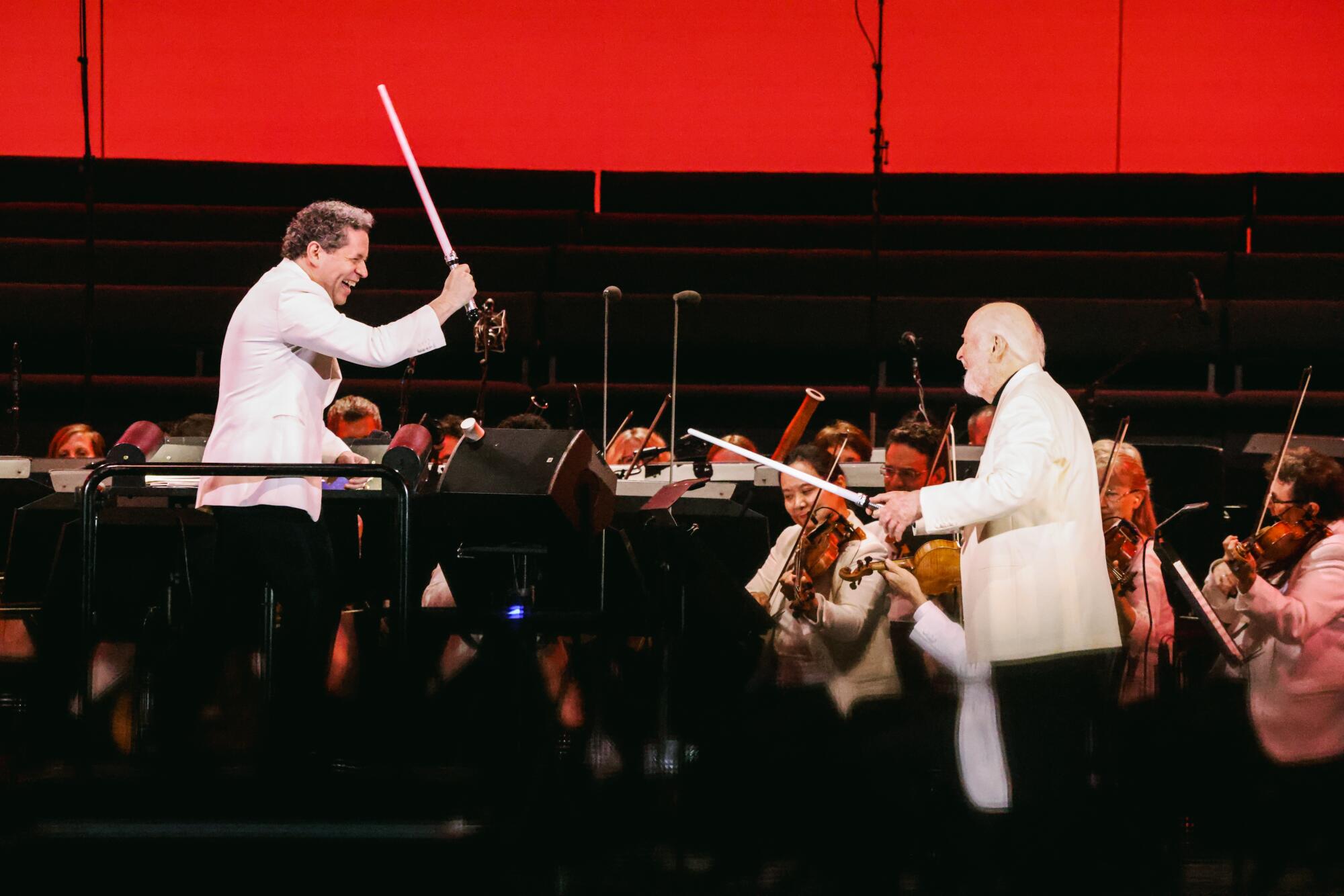 Gustavo Dudamel and John Williams hold lightsabers on stage at the Hollywood Bowl.