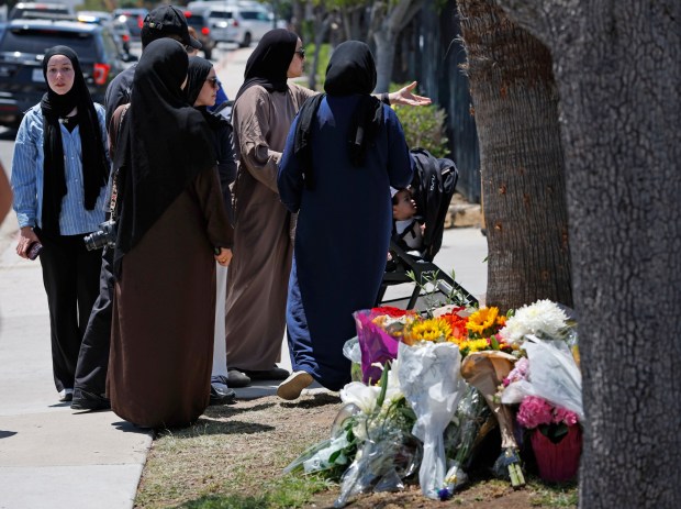 People gather next to flowers at the Islamic Center of San Diego the day after a shooting at the center left three dead on May 19, 2026 in San Diego, CA.(K.C. Alfred / The San Diego Union-Tribune)