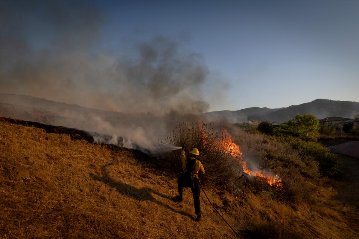 A firefighter sprays burning brush during the Sandy fire in Runkle Canyon on Tuesday.