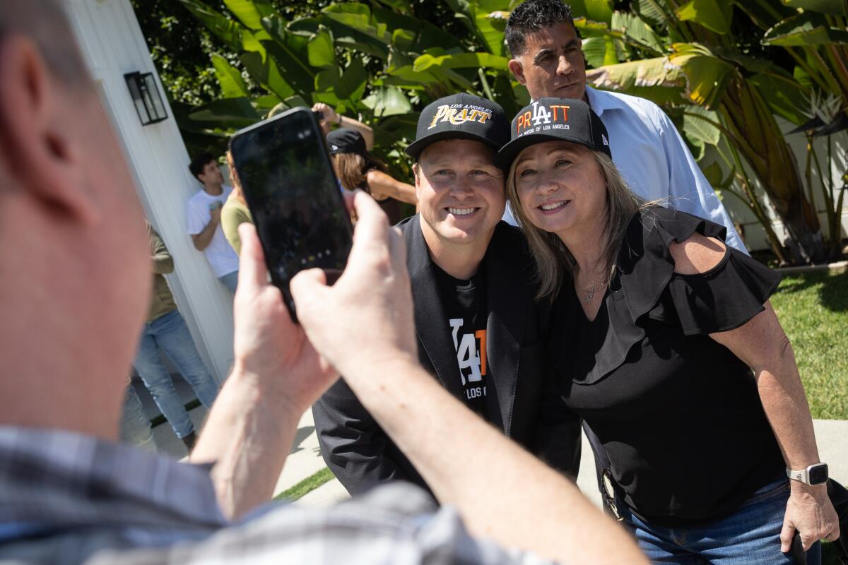 A man and a woman, both in dark ball caps that say Pratt, pose for a person taking their photograph with a cellphone 