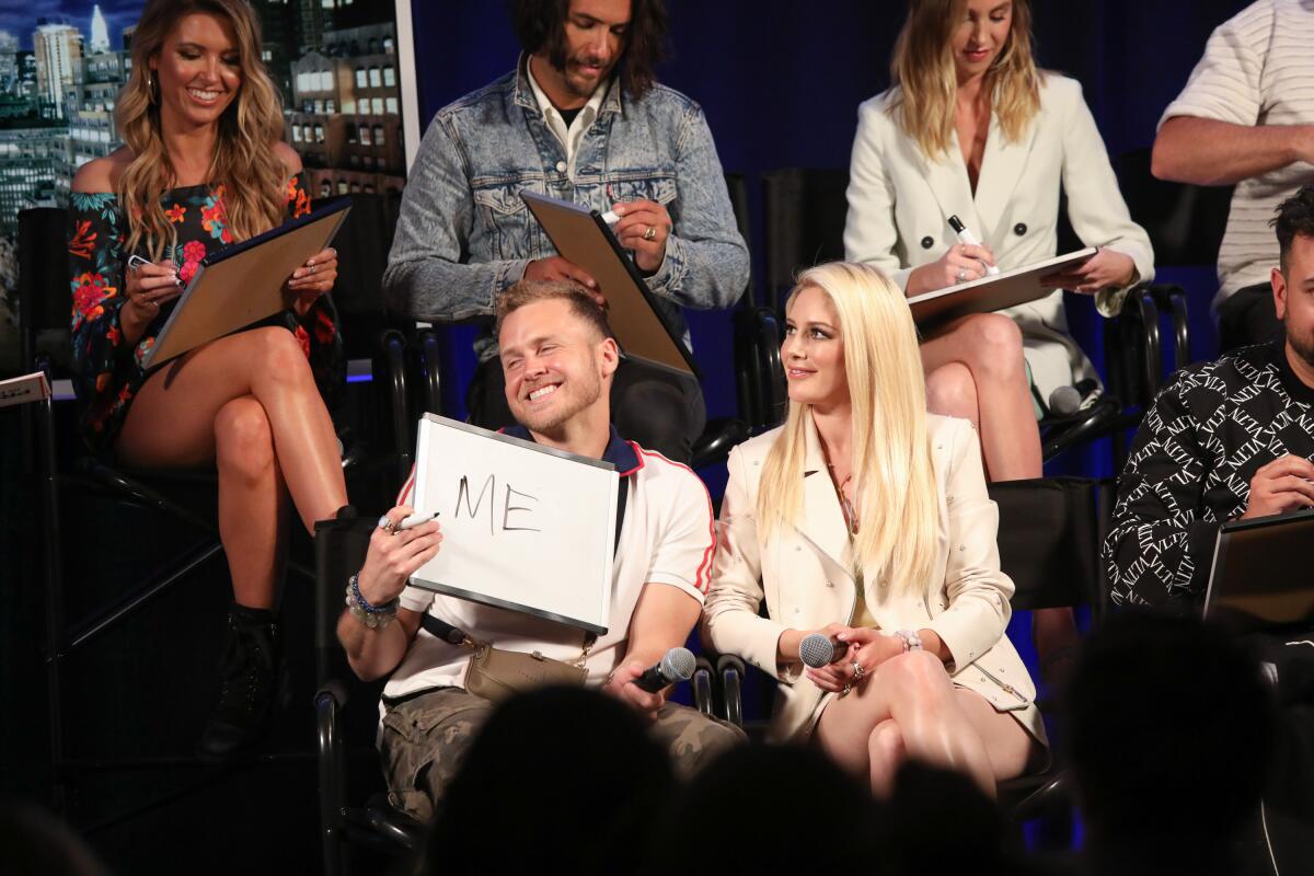 A man seated next to a blond woman holds a large white pad that says ME. Other people behind them are also holding pads
