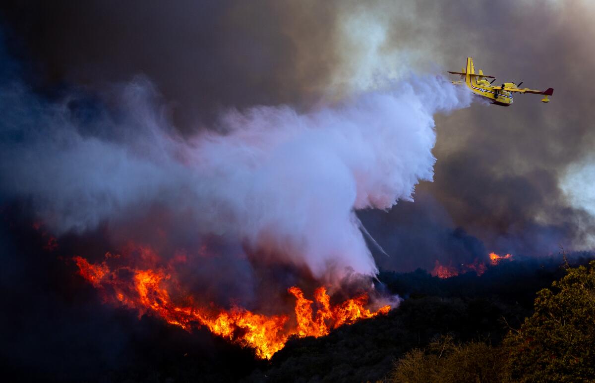 A firefighting aircraft drops ocean water on a burning hillside