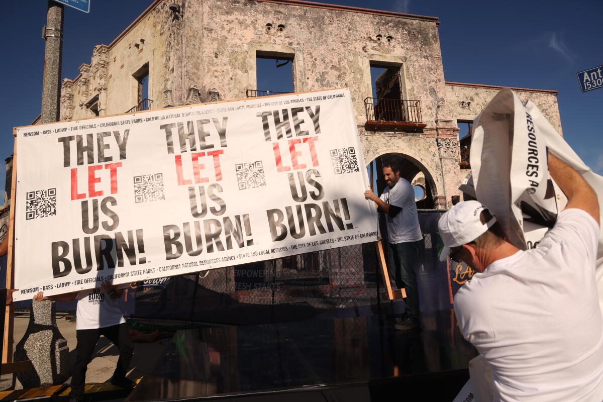 People put up a sign that repeats the words They Let Us Burn near a building with smoke marks