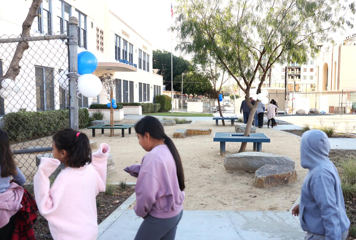 Young people walk b a school yard with trees and seating.