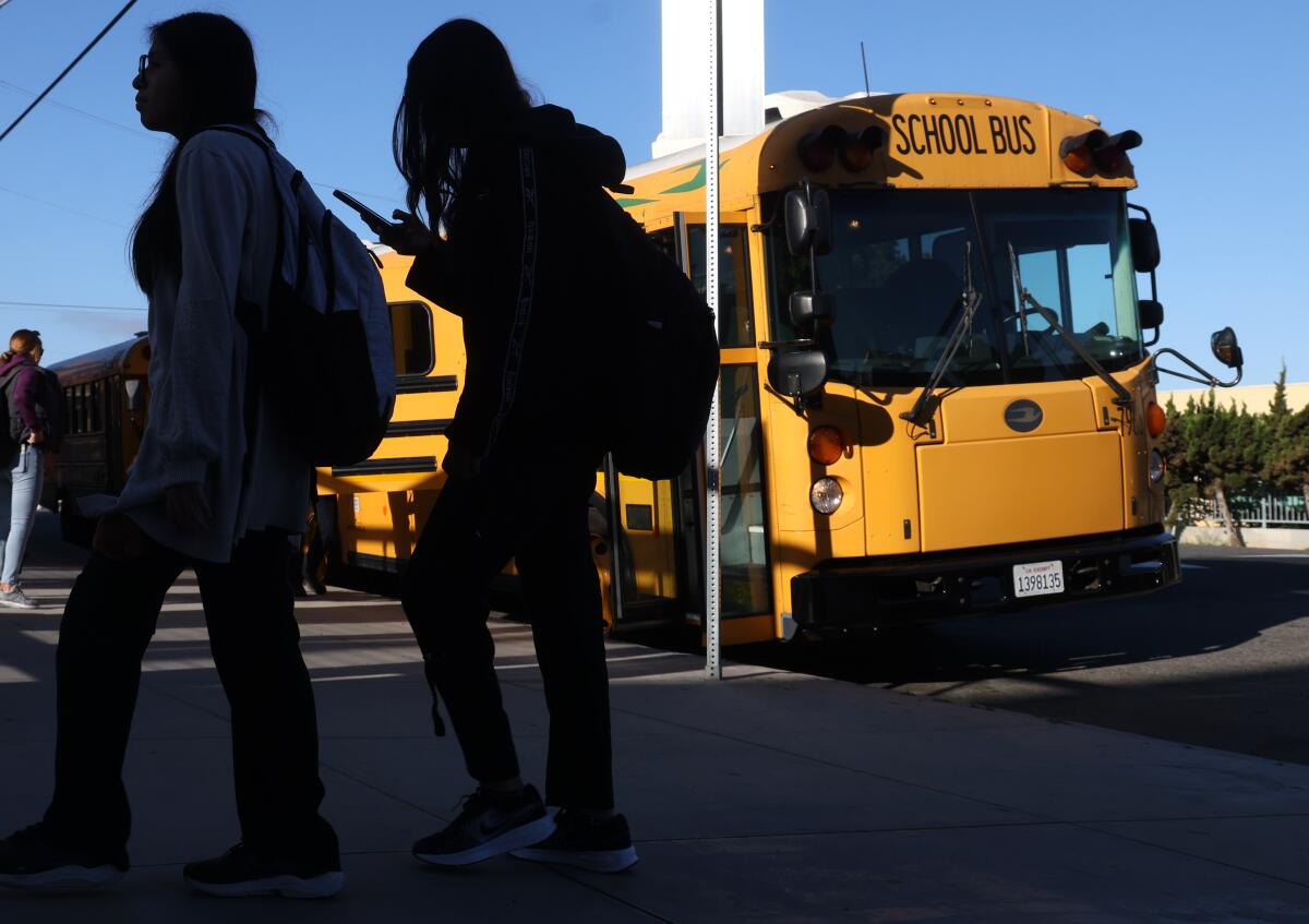 Two people walk near a yellow school bus.