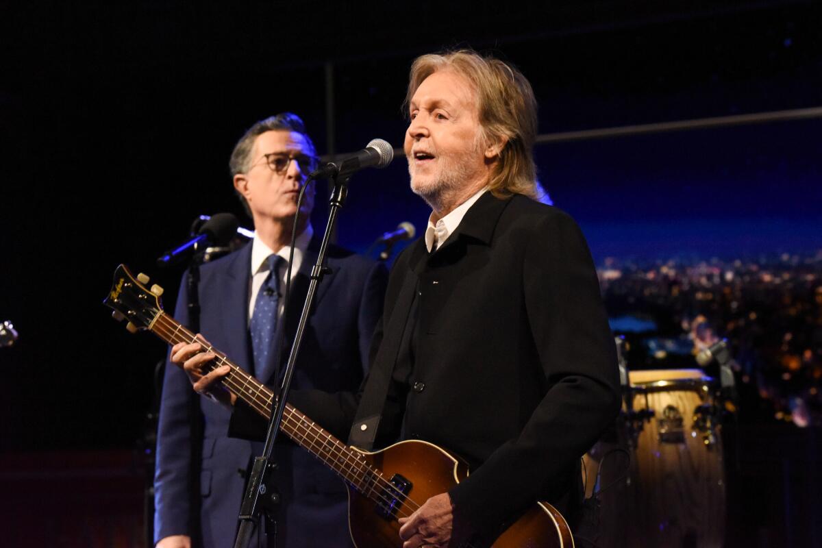 Two men on a stage at singing into microphones. One holds a guitar.