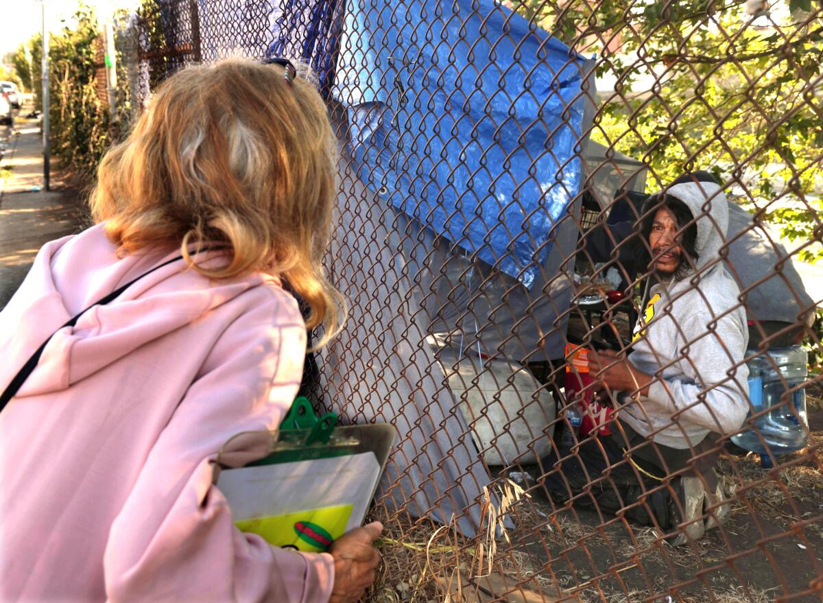 A woman talks to another across a chain linked fence