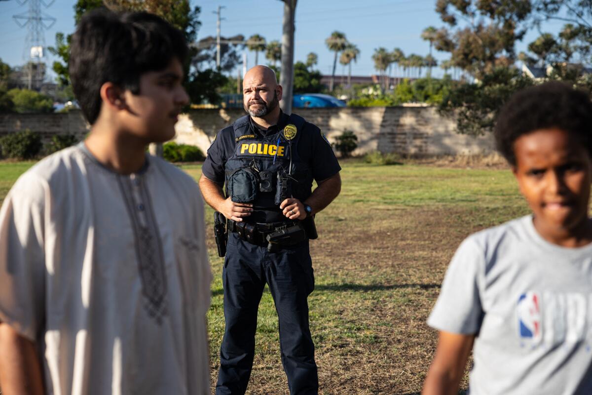 a police officer stands in a field behind and between two boys