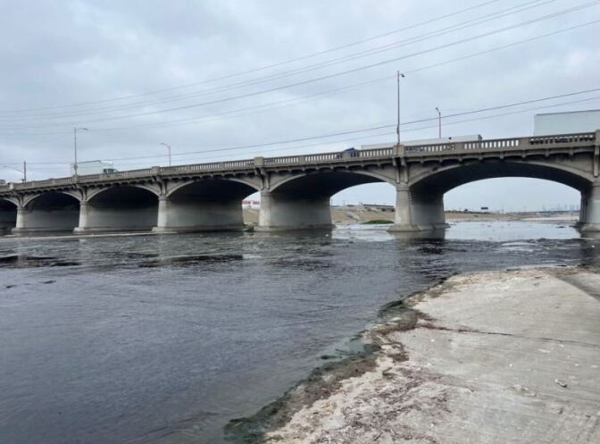 A low lying body of water running underneath a concrete bridge overpass.