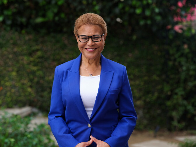 A Black woman with brown hair and glasses wears a blue suit and white shirt and smiles.
