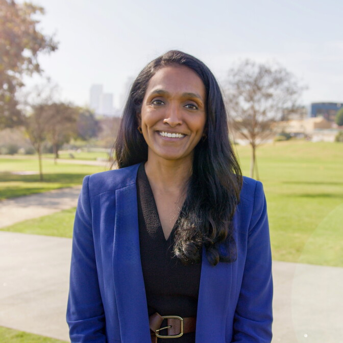 A woman smiles into the camera wearing a blue coat and black blouse