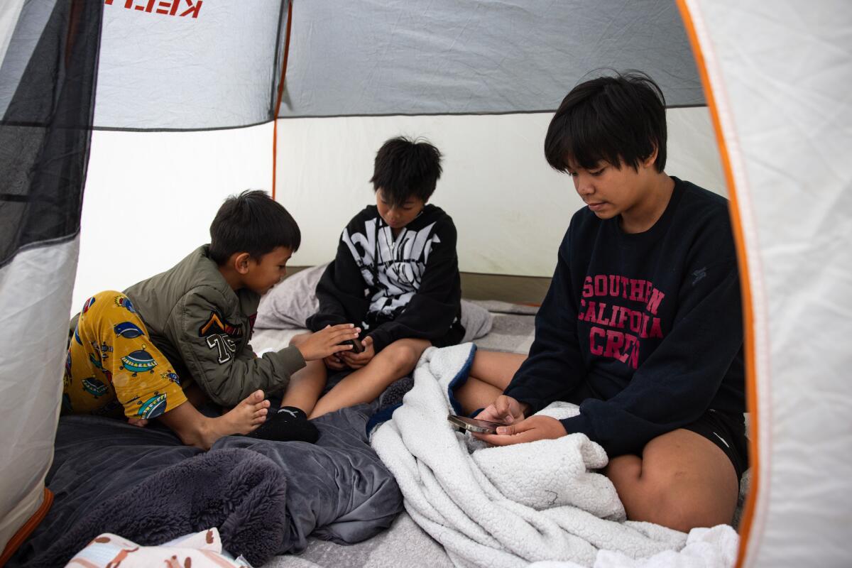 Three people look at their phones while camping outside the Freedom Hall shelter on Sunday in Garden Grove