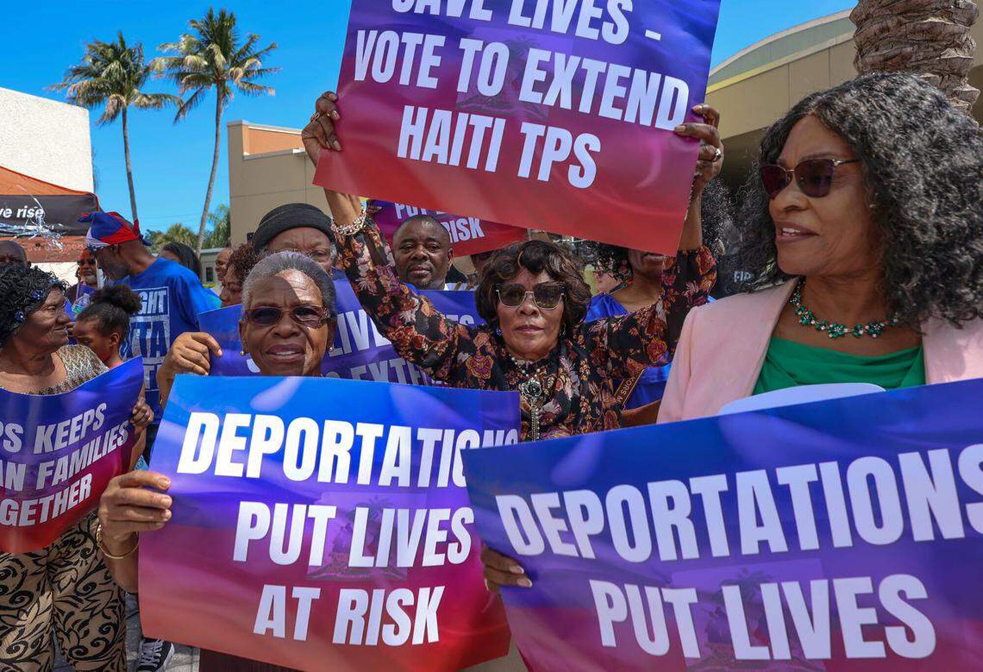 Protesters hold signs reading "Deportations Put Lives At Risk."