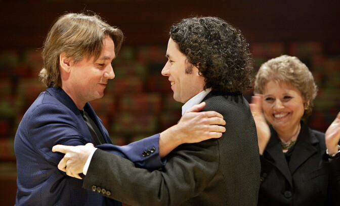 Two man hold each other by their shoulders as a woman looks on.