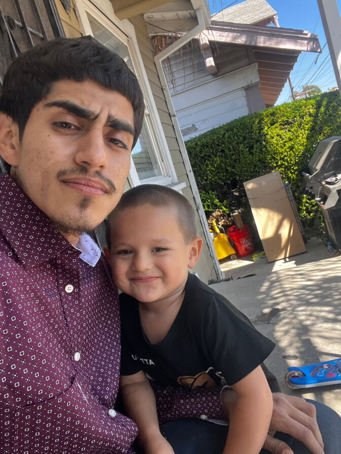 A young man with medium-tone skin wearing a burgundy shirt poses for a picture with a young boy in a black shirt.