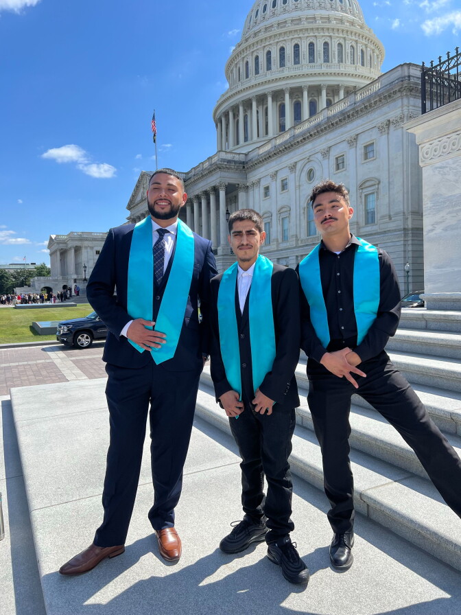 Three young men in suits and formal wear pose in front of the white Capitol building in Washington D.C.