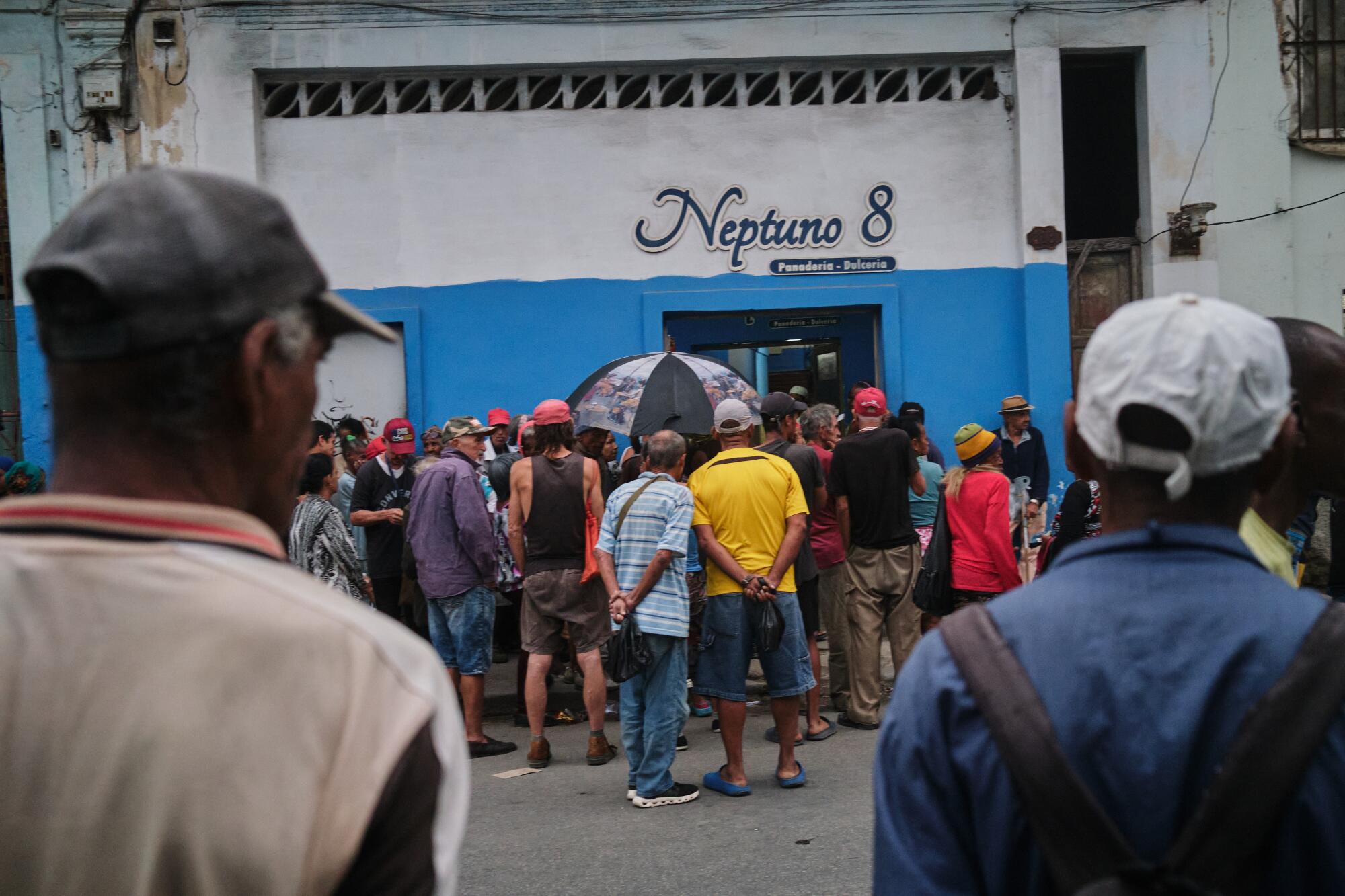 People wait in the rain outside a white and blue building with the words Neptuno 8