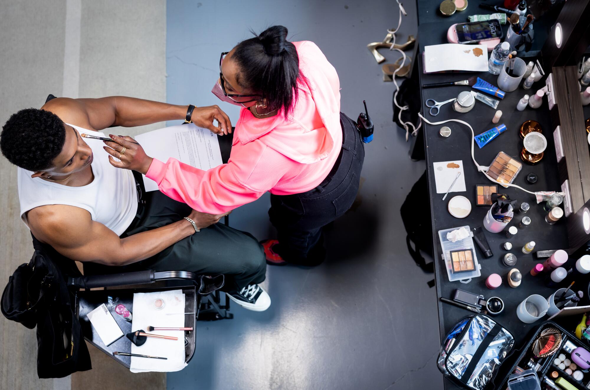 Actor Xavier Antonio Avila, left, sits while Amber Burgin touches up makeup.