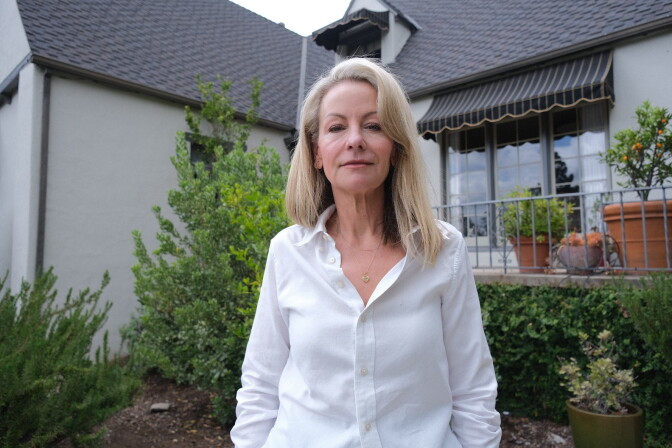 A woman with light skin tone stands in front of a two-story home in Altadena, California.