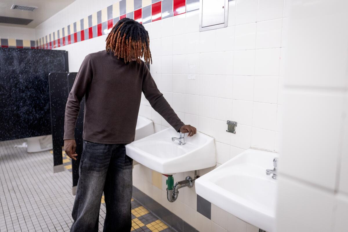 Student Zaiden Ross demonstrates a nonworking sink in a bathroom