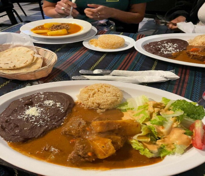 A dish with beans, a stew with meat and veggies, next to rice and a salad. Other dishes are on the table as well.