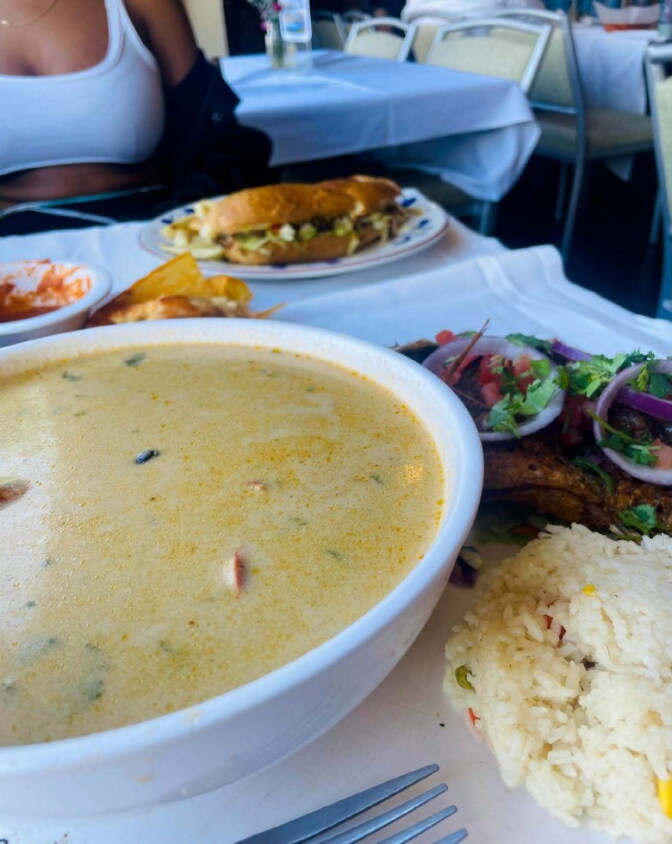 A white broth in a bowl next to a plate with some rice and salad.
