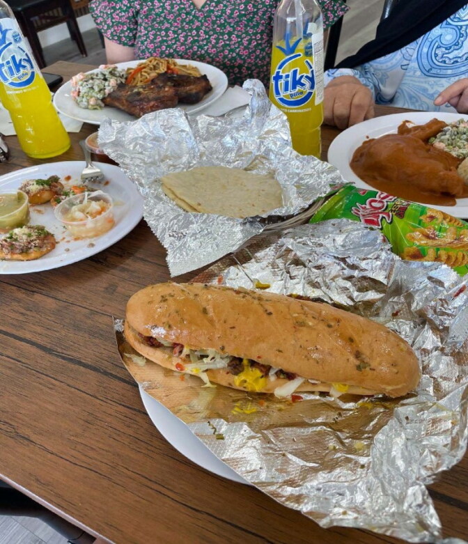 A sandwich on a foil wrapper next to snacks and plates with food on them.