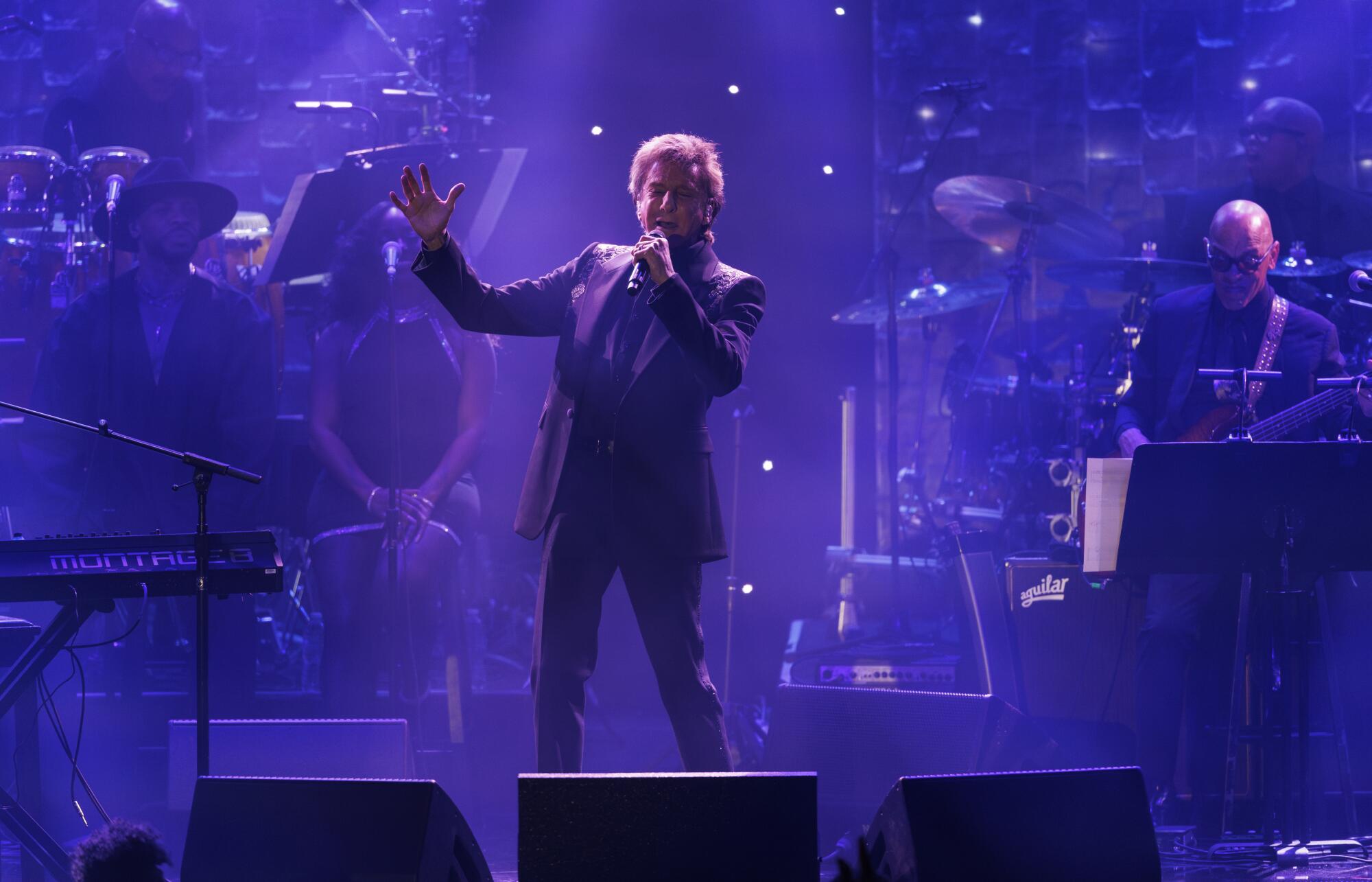 Barry Manilow performs on stage under purple lights. 