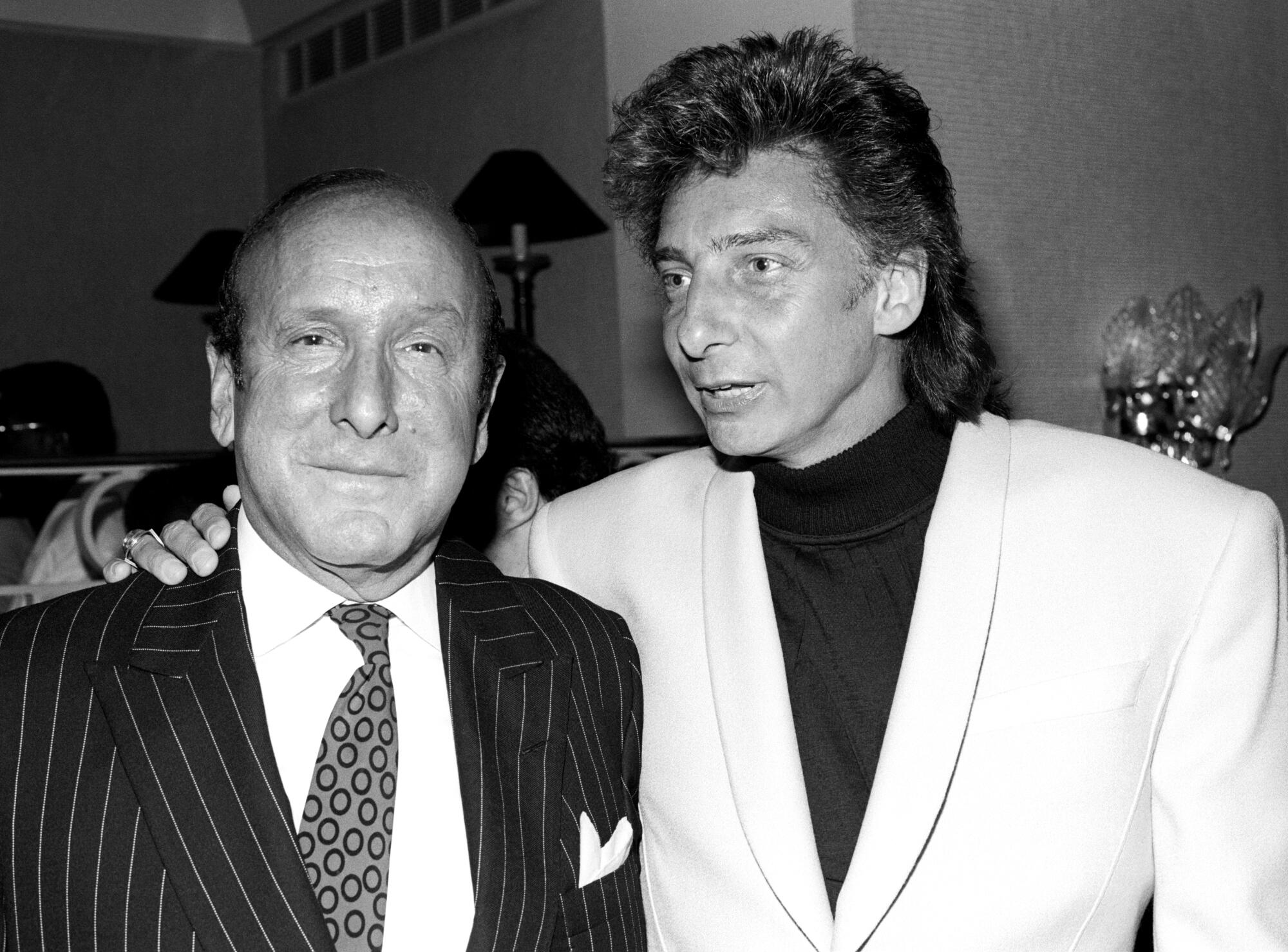 Clive Davis stands as Barry Manilow puts his hand beside his neck.