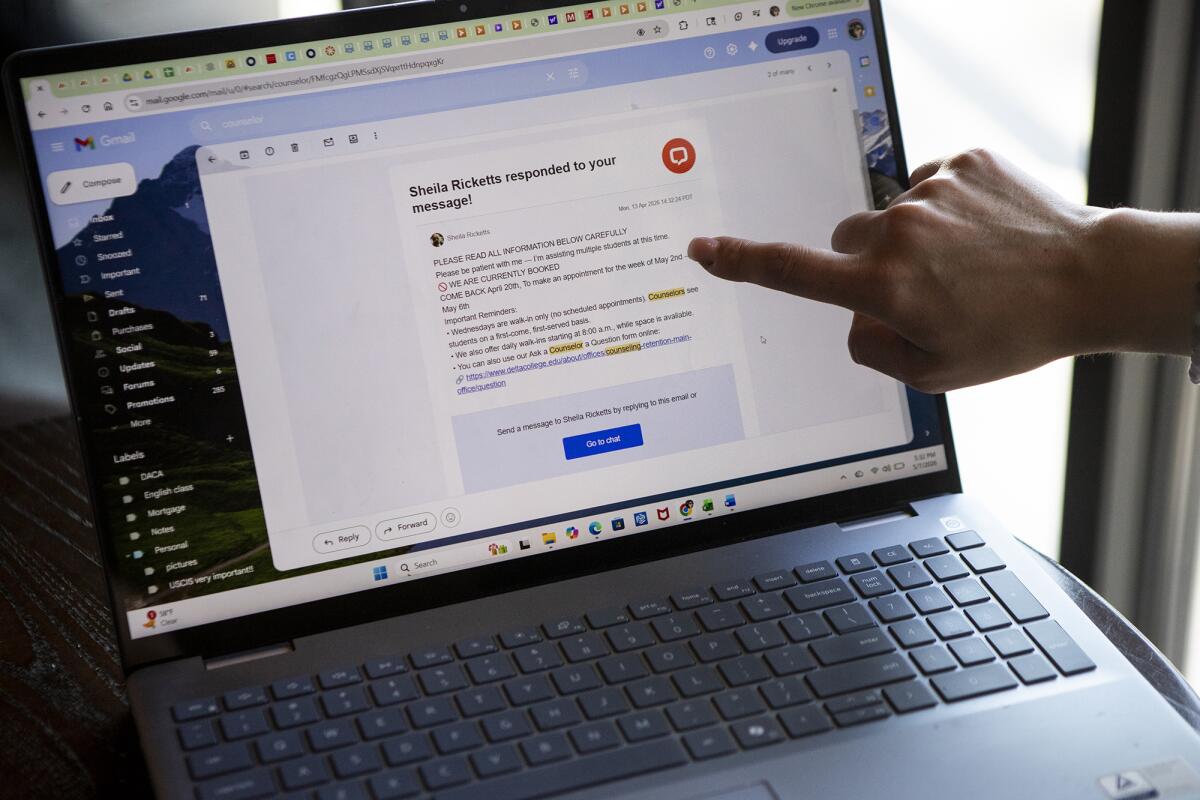 A close-up shot of a person's hand pointing toward a laptop screen displaying an email on a small table in a restaurant.