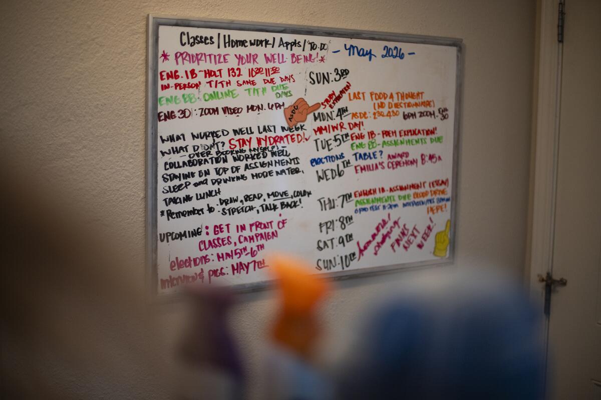 A view of a whiteboard with a schedule written on it in various colors of marker hanging on the wall of an entryway of a house.