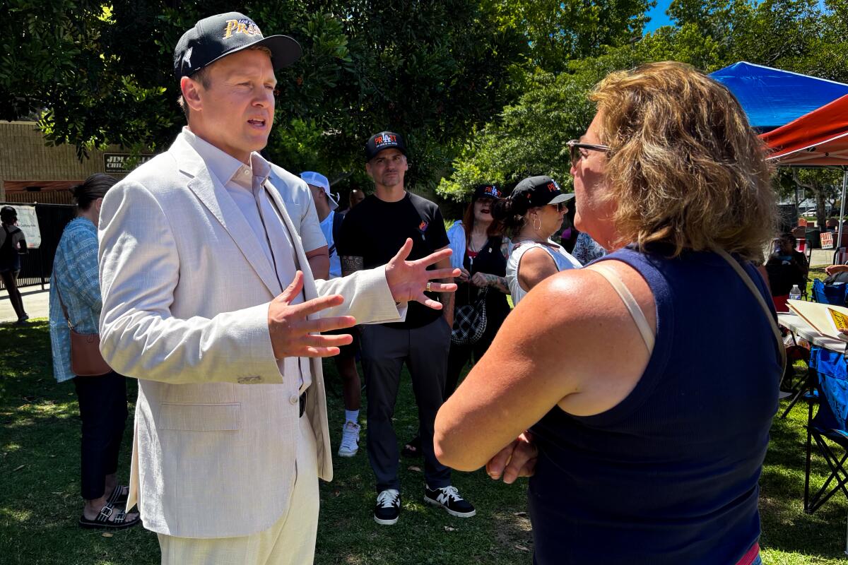 Spencer Pratt, in a beige suit, speaks to a woman at an outdoor event.