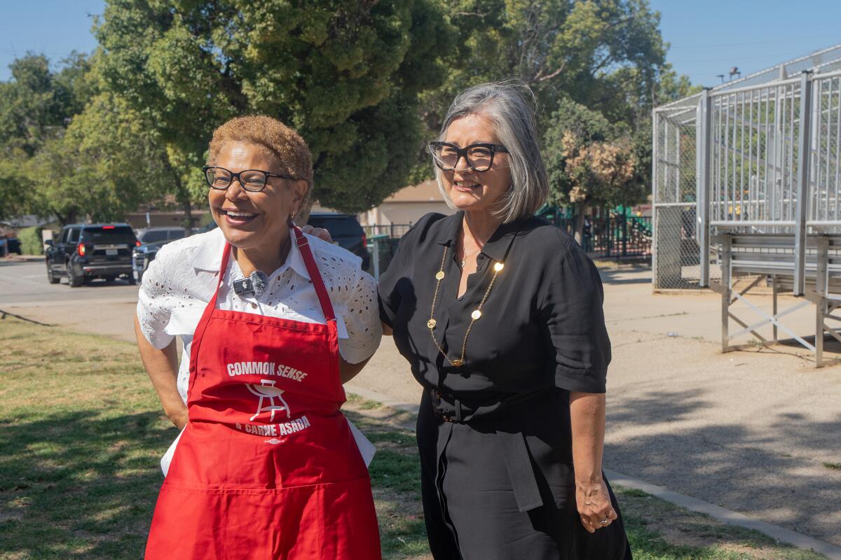 Mayor Karen Bass wears a red apron and stands next to Monica Rodriguez.