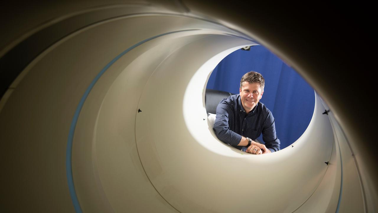 Simon Cherry framed inside the open end of a large white pipe, a PET scanner