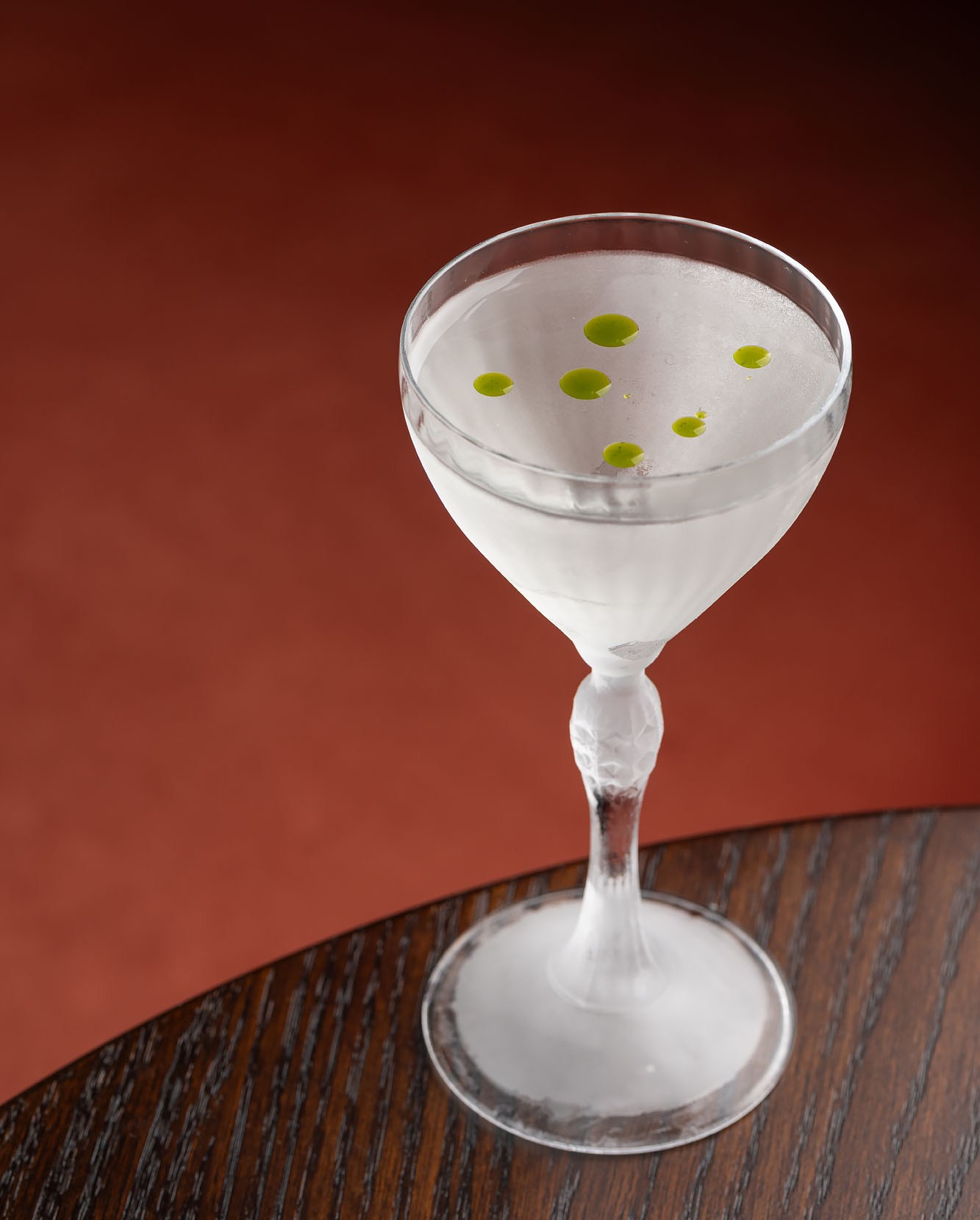 Martini in a clear glass with drops of green on a dark wood table at Firstborn.