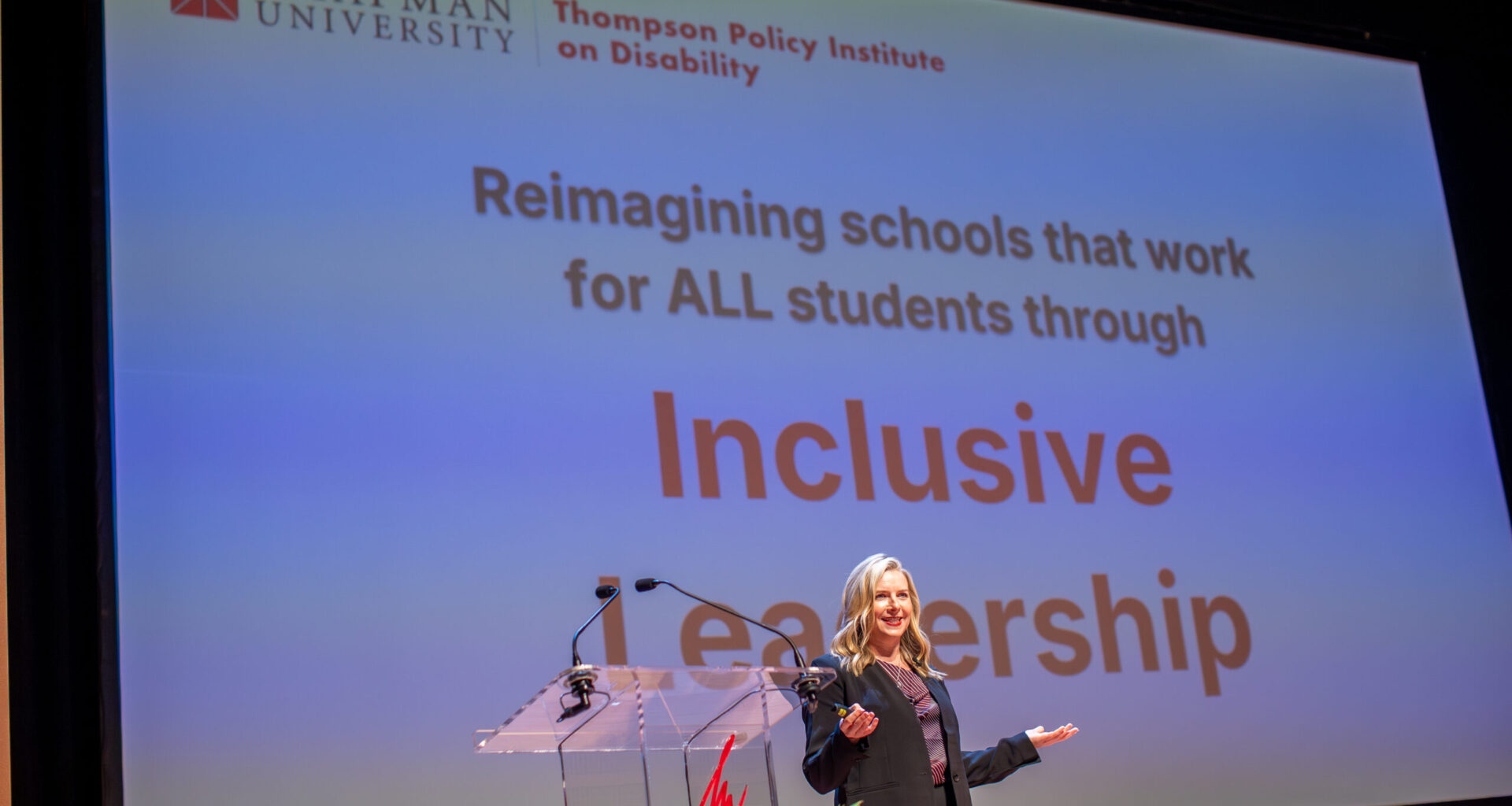 Kari Adams speaks onstage at the 2025 Thompson Policy Institute Summit on Disability and Inclusion at Chapman University, standing in front of a presentation screen displaying the words “Inclusive Leadership.”