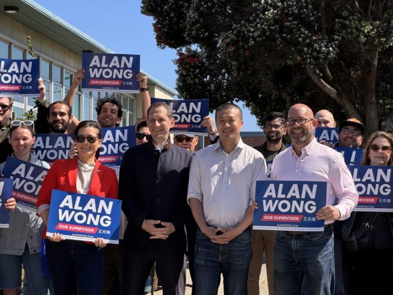 A group of people stand outdoors holding "Alan Wong Our Supervisor" signs, showing support for a political candidate.