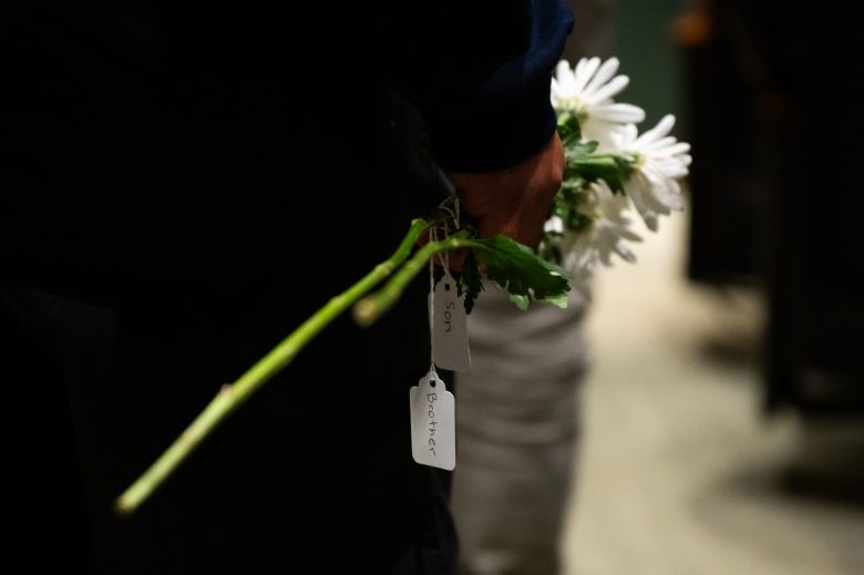 Hand holding daisies with tags reading "Son" and "Brother."
