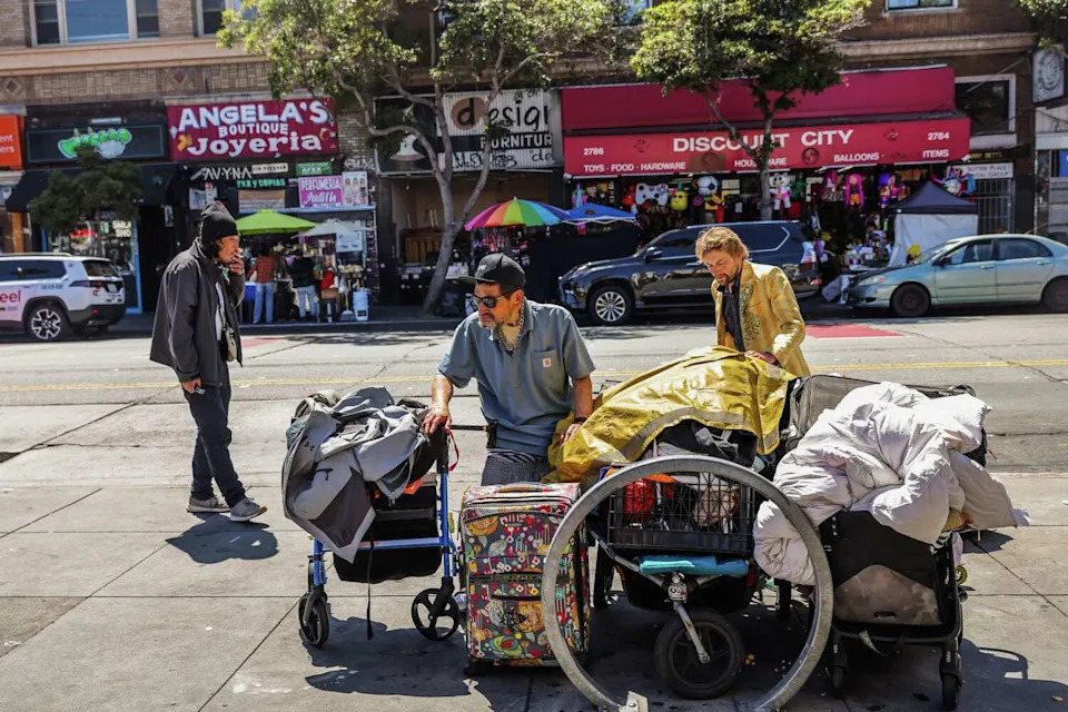 Pete, 55, center, and his friend Zach, 42, who is homeless, right, gather belongings that they illegally sell on Mission Street near 24th Street in San Francisco. They said they've been selling items in the area for several years. (Gabrielle Lurie/S.F. Chronicle)