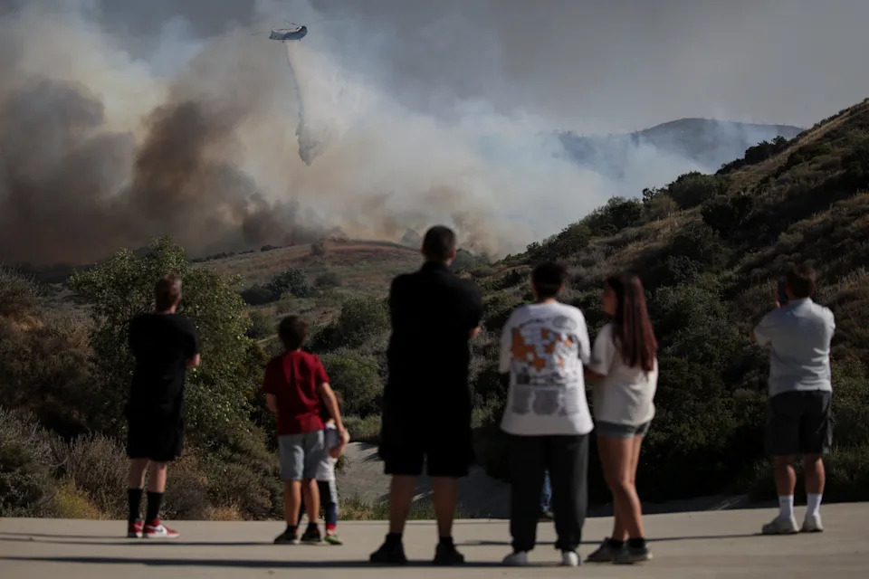 People watch as a firefighter helicopter battles a wildfire known as the Sandy Fire, in Simi Valley, Calif., May 18, 2026.
