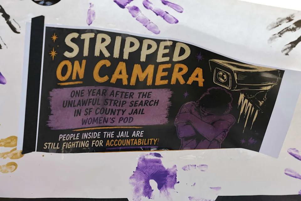 A banner reads "Stripped on Camera" during a vigil to honor survivors of an alleged mass strip search at the San Francisco County Jail on May 22, 2026, in San Francisco. (Lea Suzuki/S.F. Chronicle)