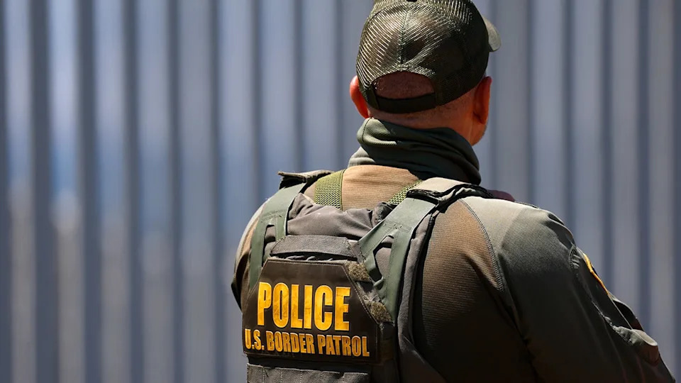U.S. Customs and Border Protection agent standing at Border Field State Park with border wall in background