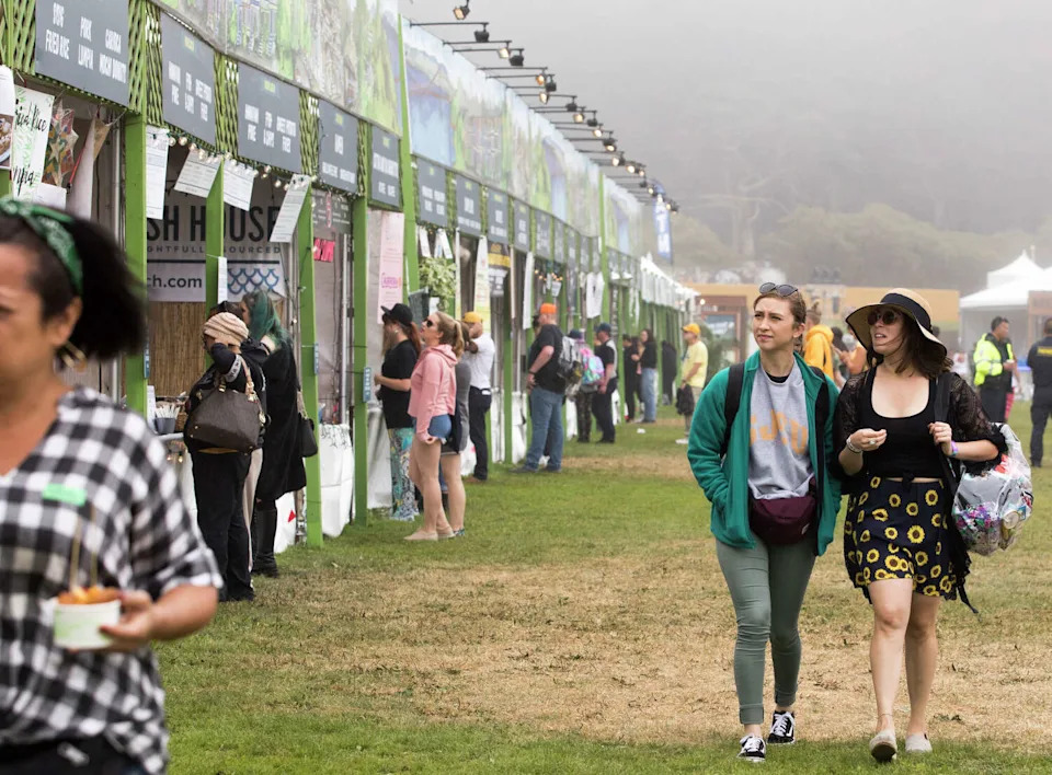 Two festival attendees check out a row of food vendor options at Outside Lands in San Francisco's Golden Gate Park. The festival's 2026 food and drink lineup will feature 100 Bay Area restaurants. (Jessica Christian/The Chronicle)