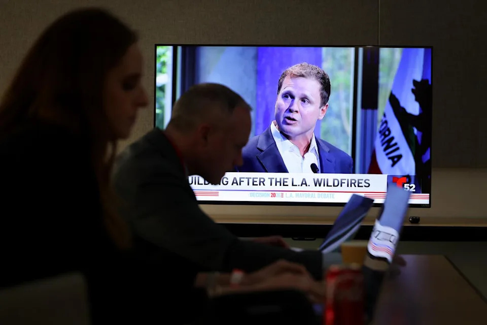 Spencer Pratt is shown on a television while journalists work during the 2026 Los Angeles mayoral debate.
