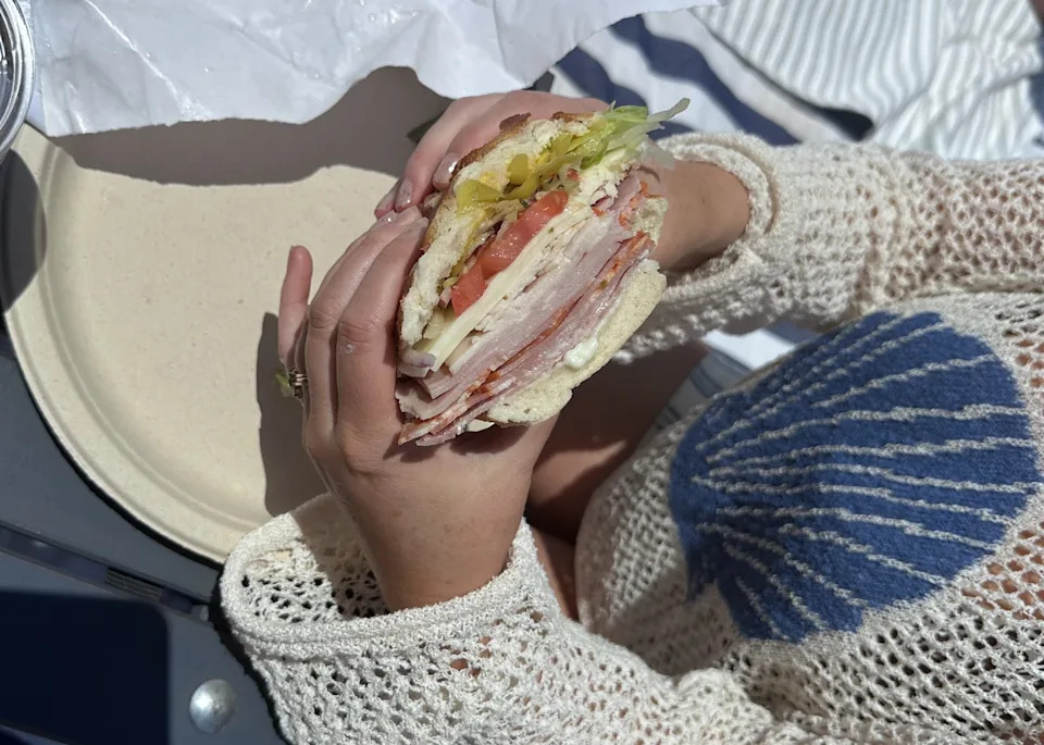 Two hands holding a Cricca’s sandwich on the beach