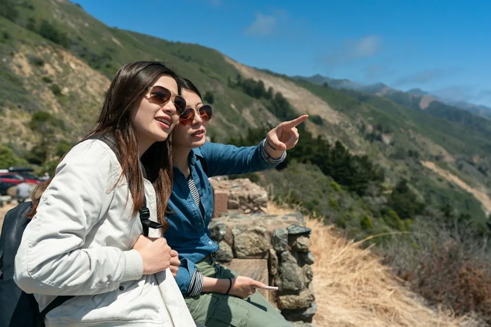 Two female tourists in sunglasses pointing at a landmark in Big Sur. PR Image Factory – stock.adobe.com