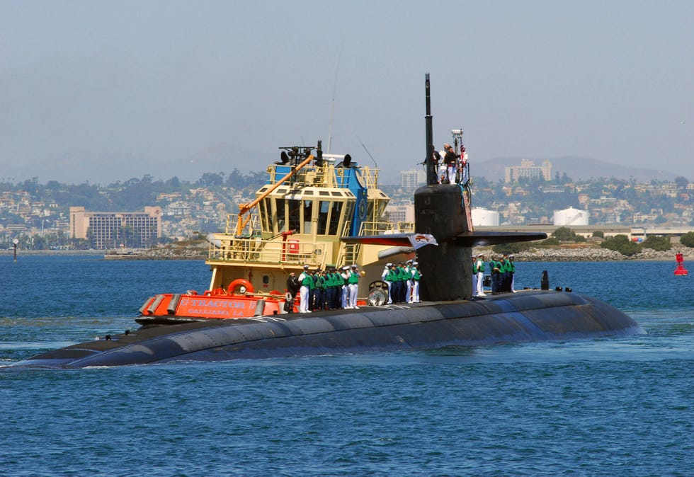 Submarine being guided by a tugboat in a harbor.