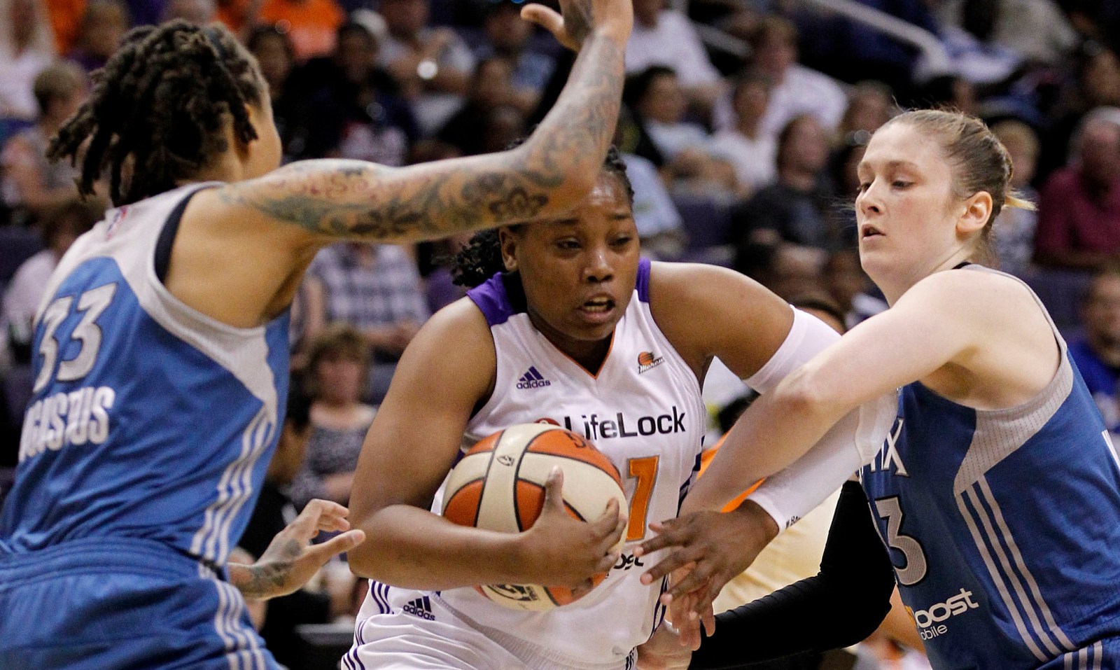 A basketball player in rough traffic, with opponents on either side of her.