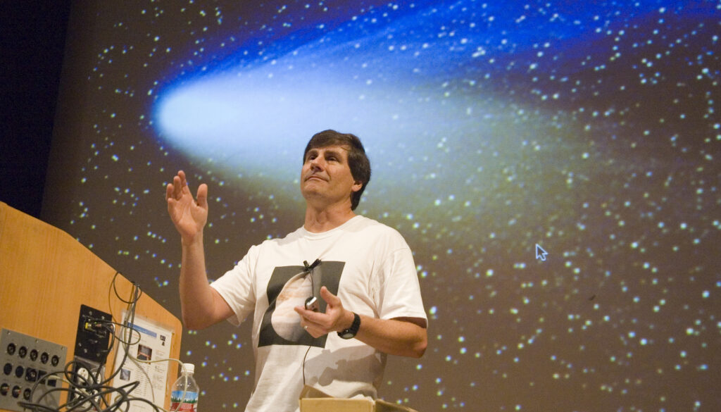 a man gesticulating in front of a picture of a comen