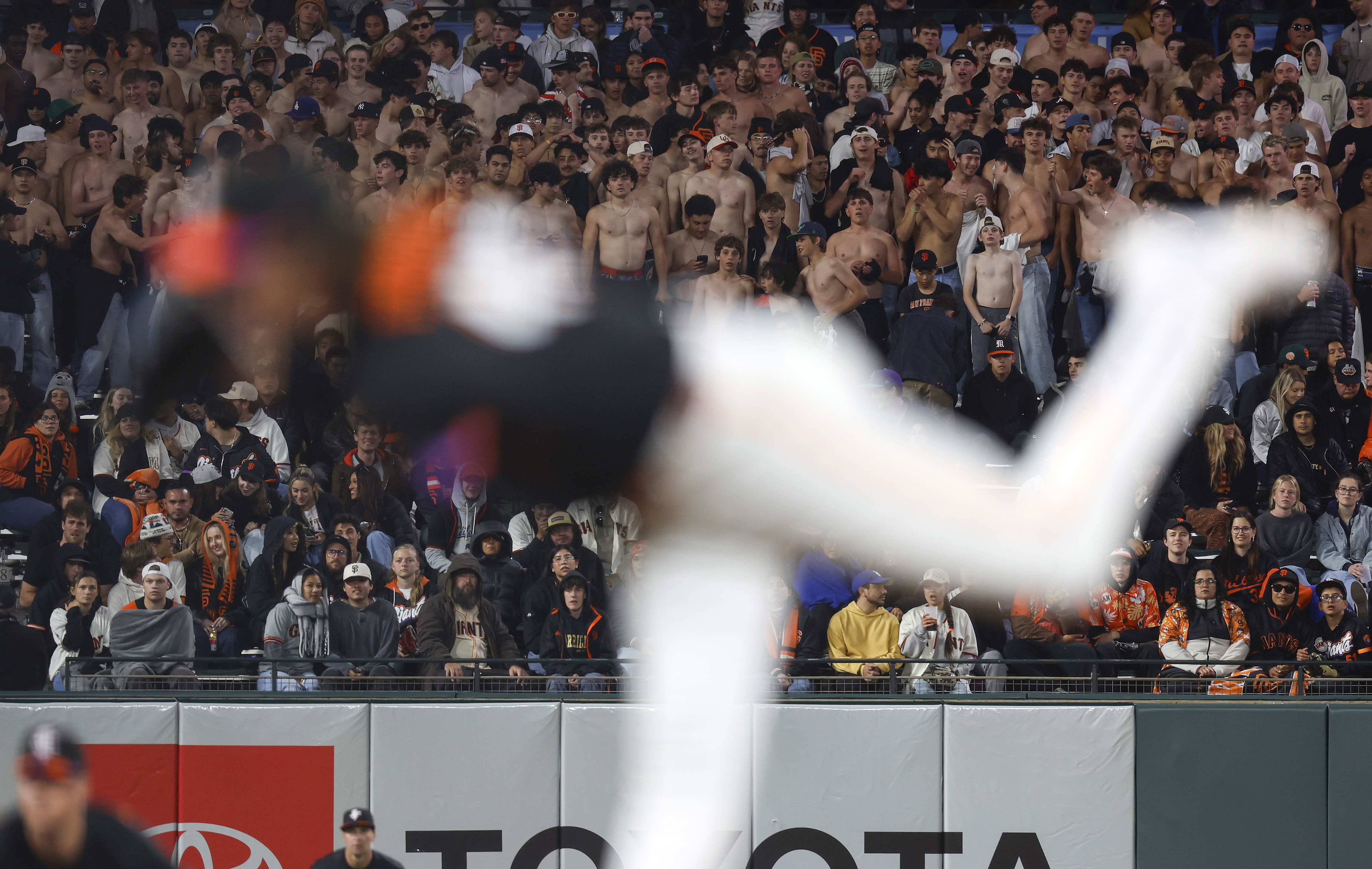 Fans in the left field bleacher seats stand shirtless as...